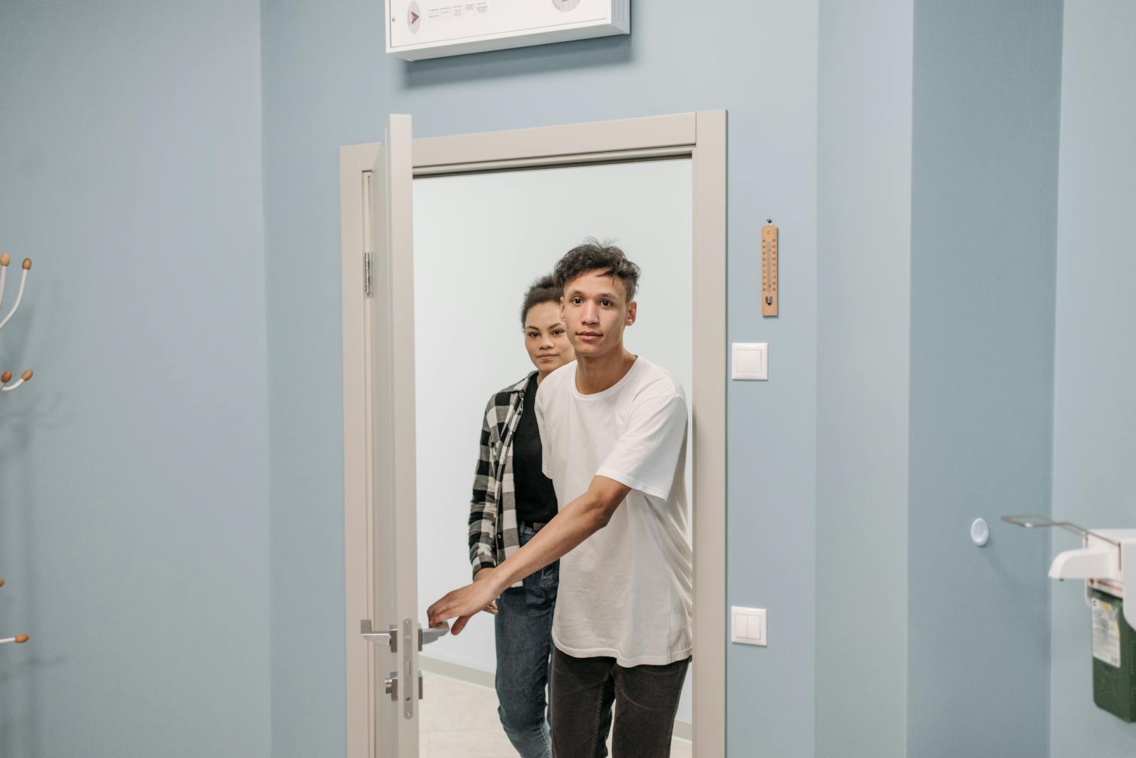 A young couple stepping through a modern doorway into a well-lit room with a light blue wall.