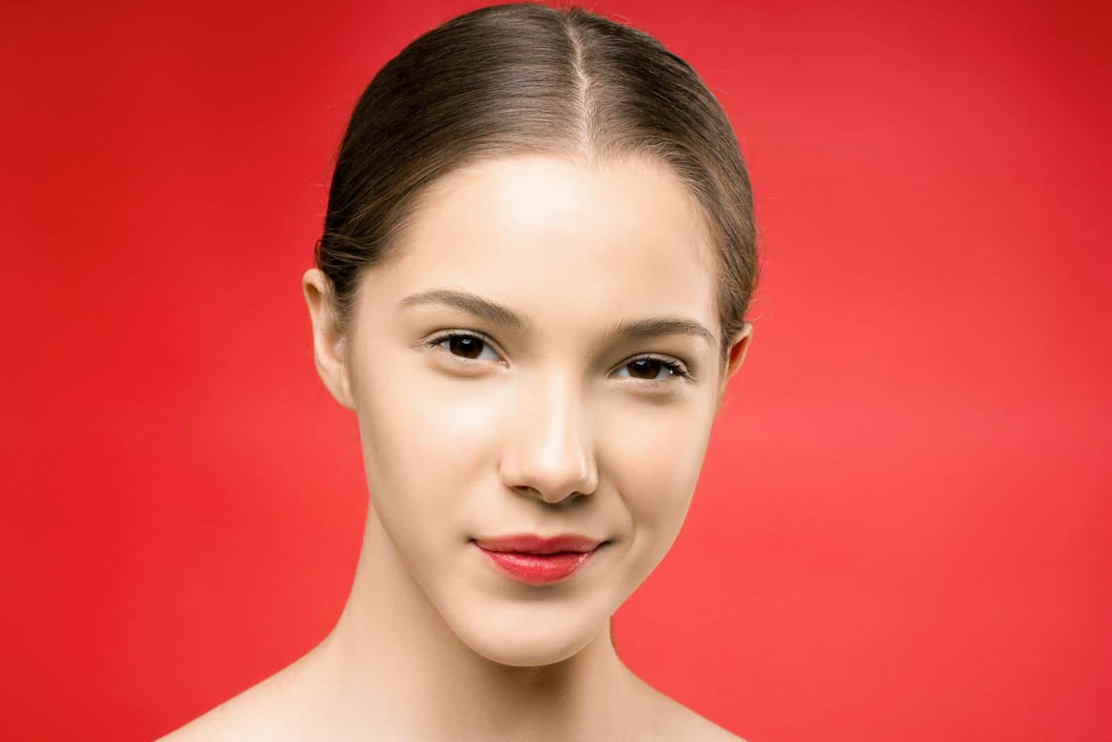 A young woman with red lipstick poses gracefully against a vibrant red backdrop.