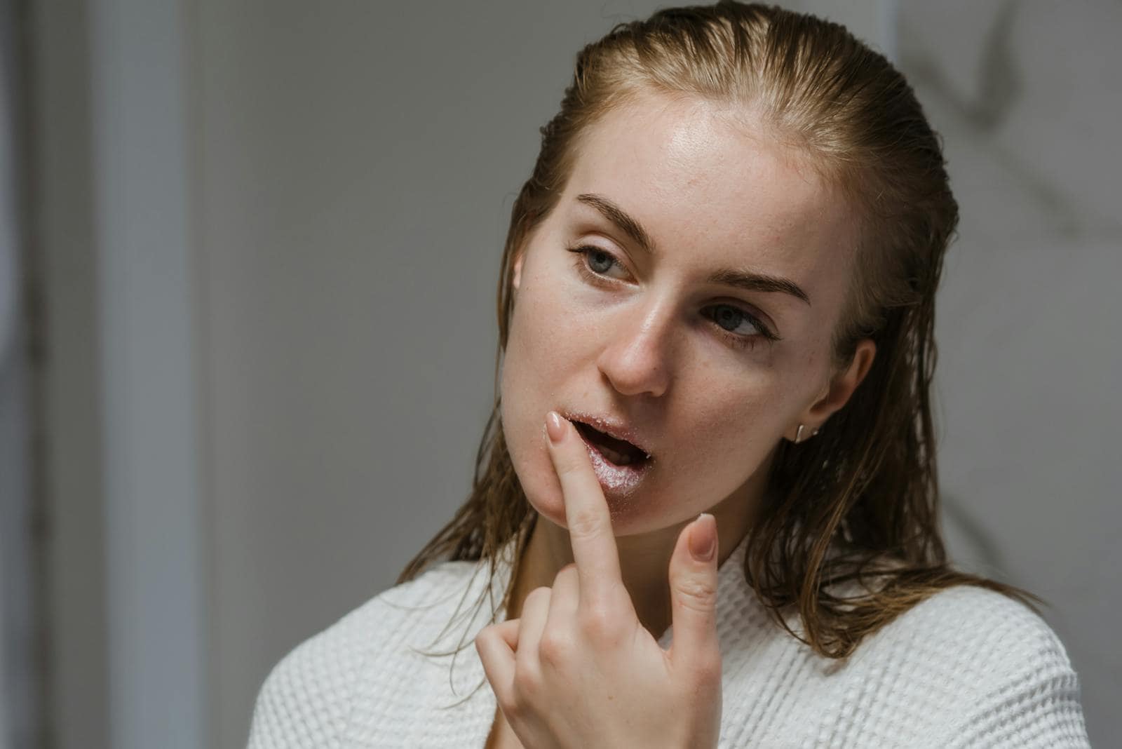 Adult woman applying a lip scrub as part of her beauty routine indoors.