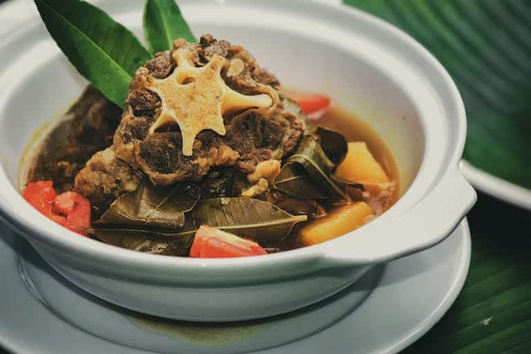Appetizing oxtail soup from Jawa Timur, Indonesia, in a white bowl with colorful vegetables and spices.