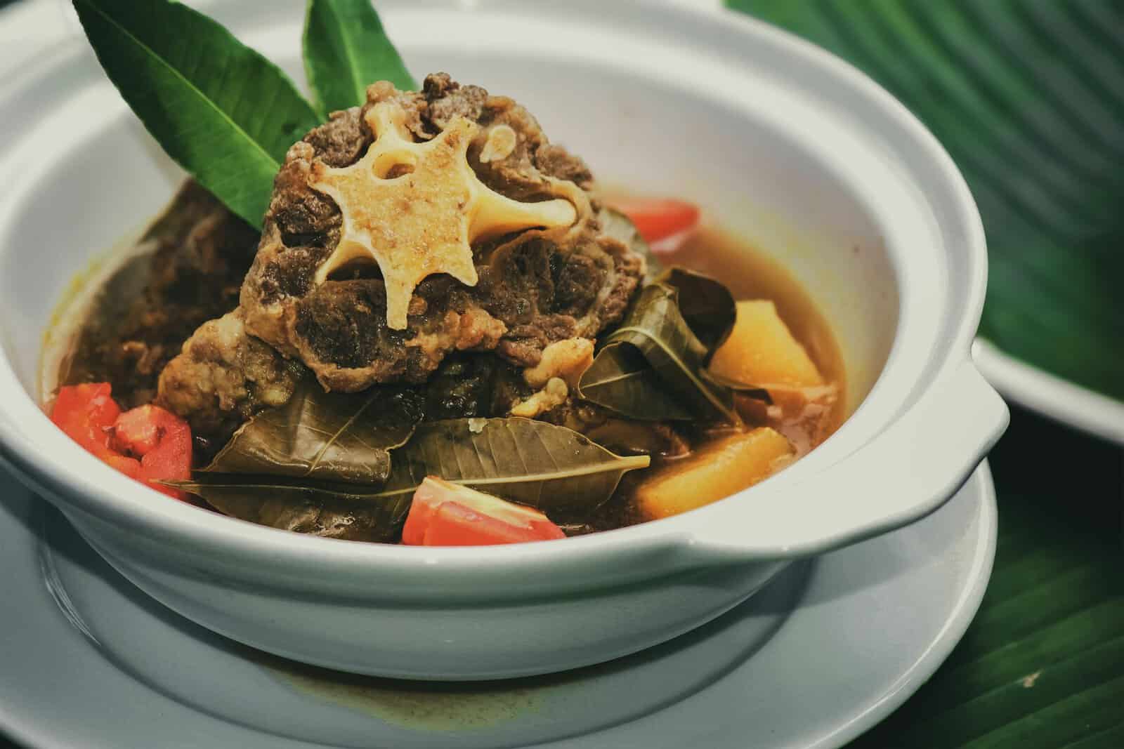 Appetizing oxtail soup from Jawa Timur, Indonesia, in a white bowl with colorful vegetables and spices.