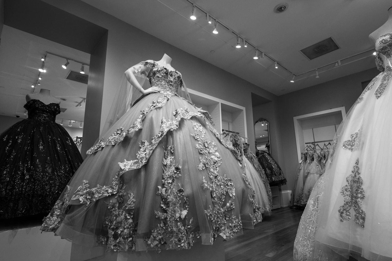 Black and white image of elegant ball gowns displayed in a boutique, showcasing intricate details and design.