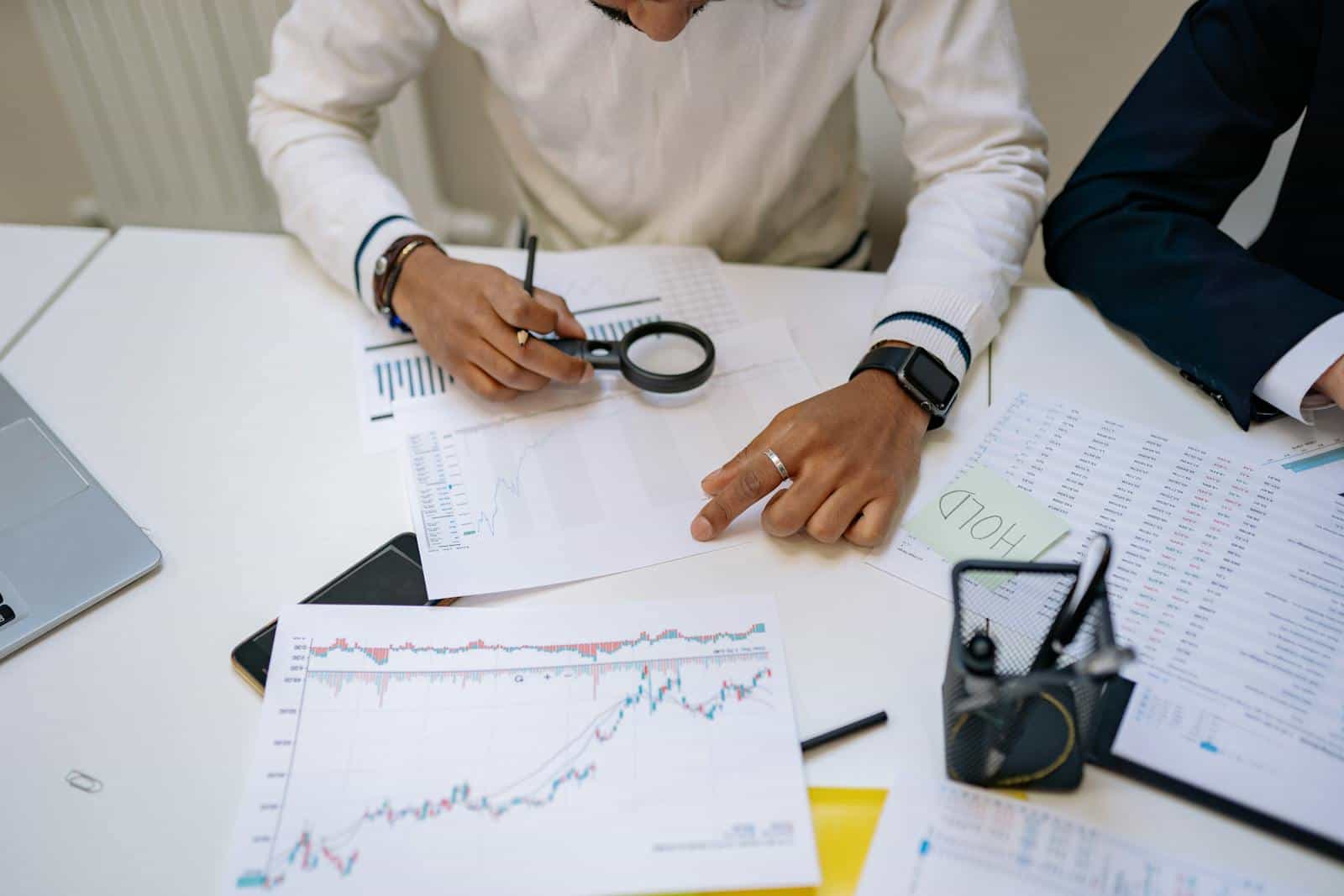 Business professionals reviewing charts with a magnifying glass in an office setting. Operations Research Analyst