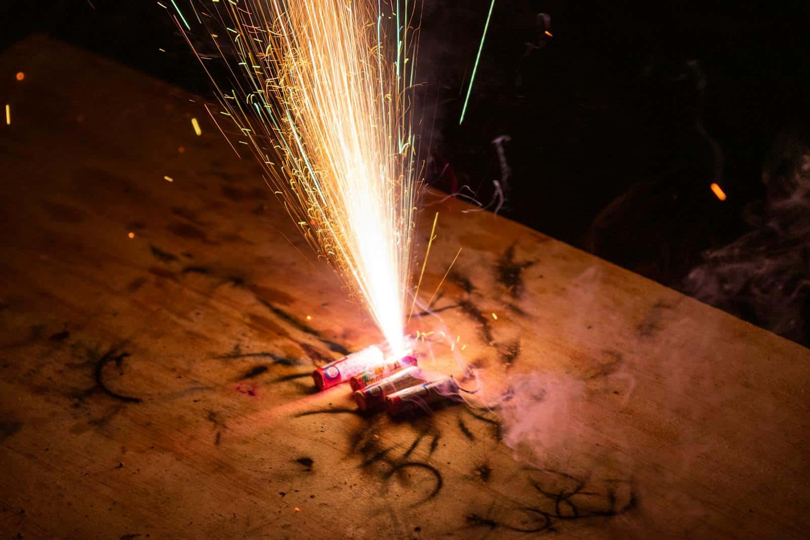 Close-up of a firecracker on wood emitting bright sparks and smoke.