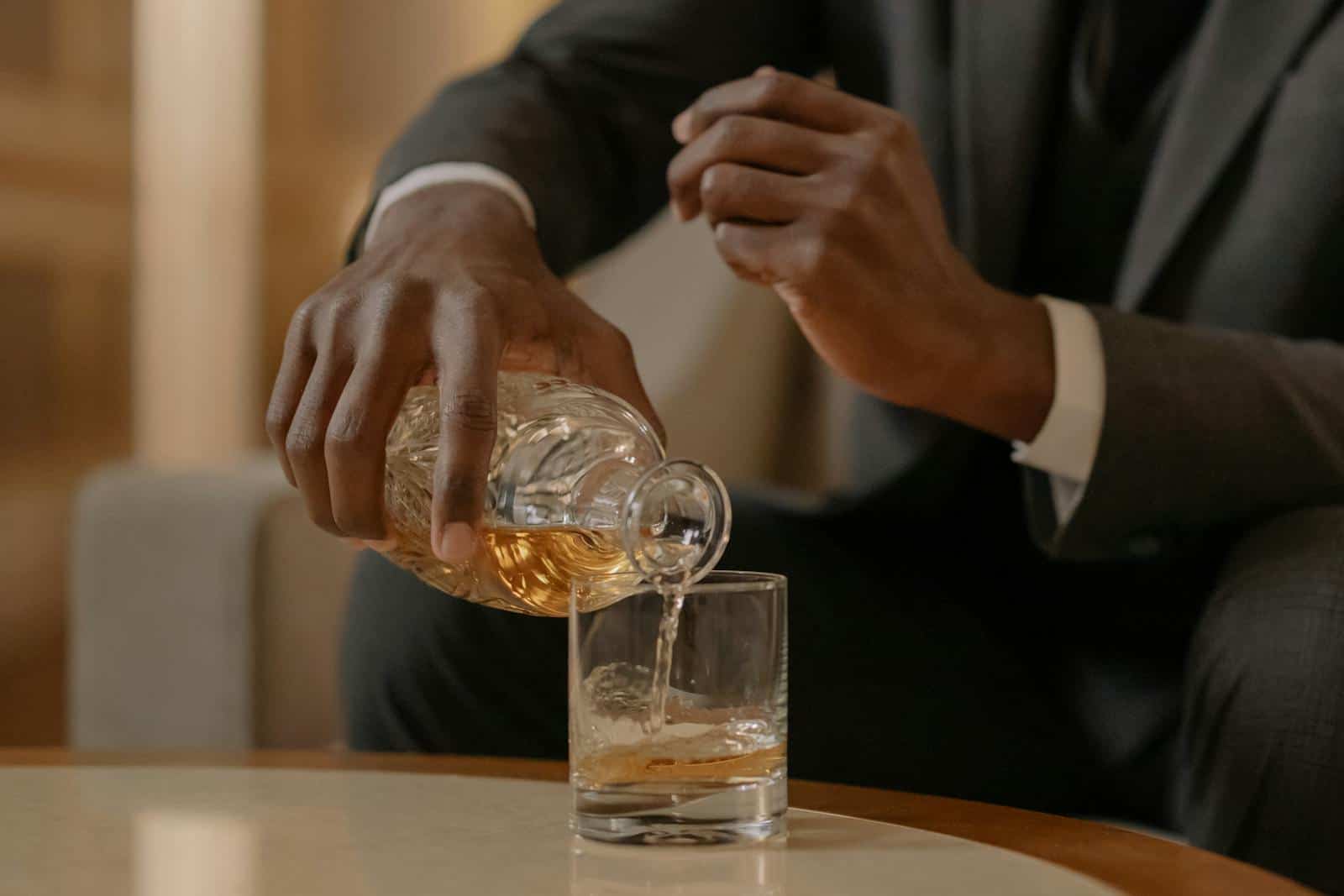 Close-up of a man elegantly pouring whiskey into a glass at a luxurious indoor setting.