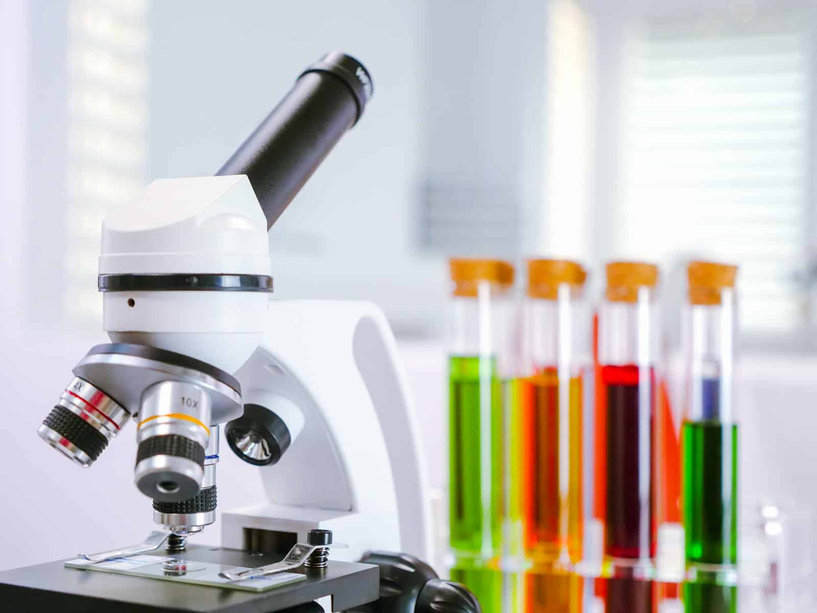 Close-up of a microscope with colorful test tubes in a laboratory setting.