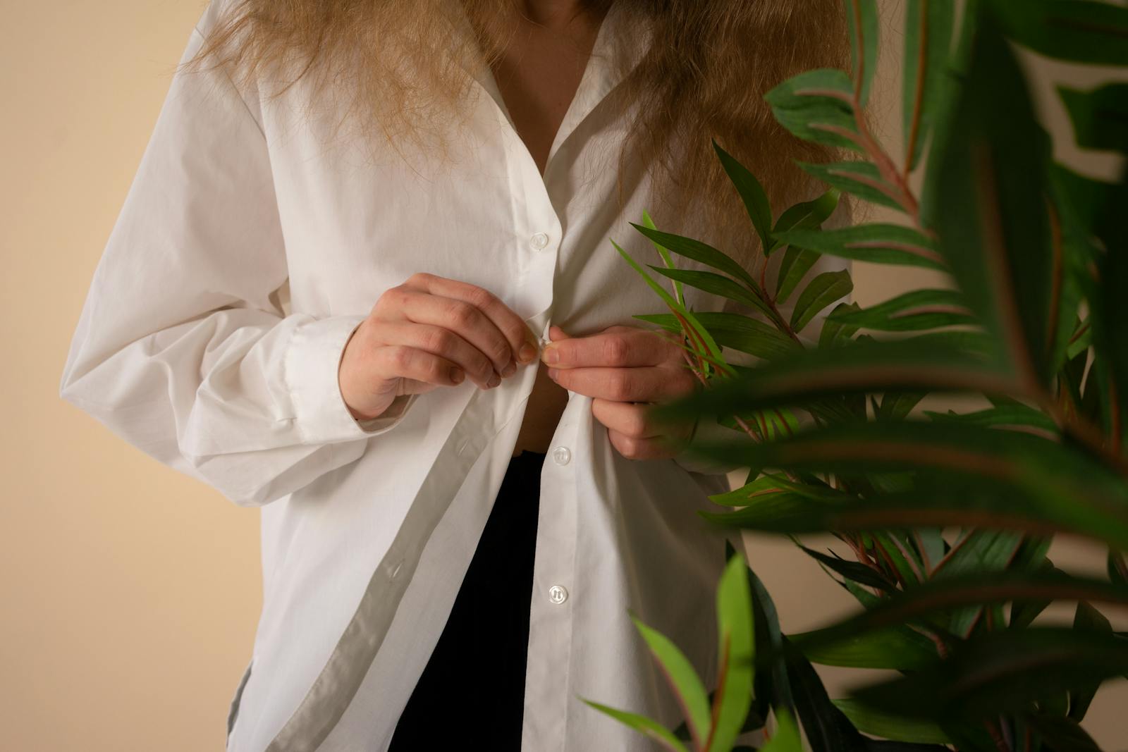 Close-up of woman buttoning shirt with indoor plant, cozy textile fashion.