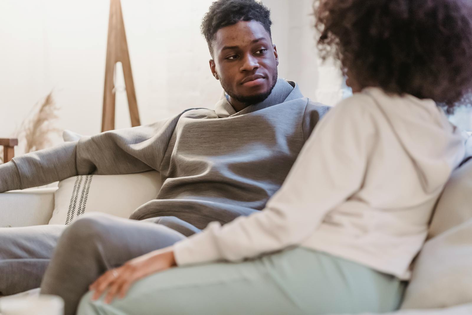 Crop African American boyfriend listening ethnic anonymous girlfriend while relaxing on sofa in lounge