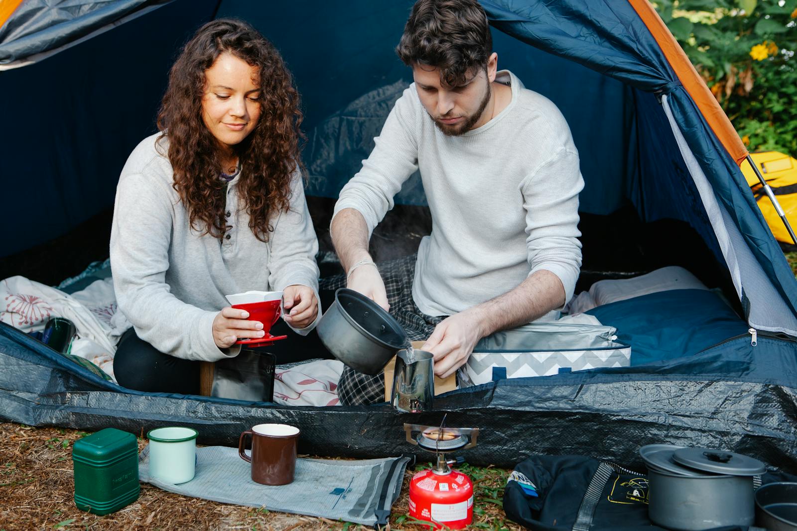 Crop young male tourist pouring hot water in pitcher near girlfriend with filter for coffee in campsite