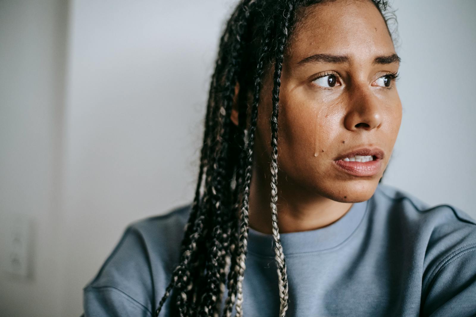 Crop young unhappy African American female with Afro braids in casual clothes looking away in house