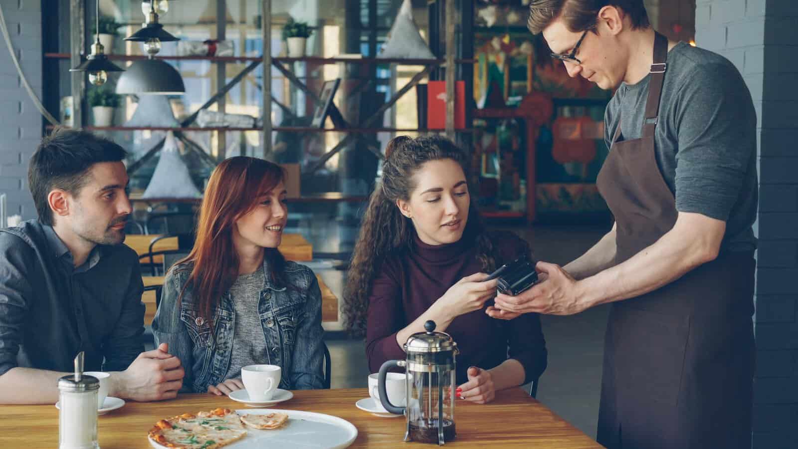 Group of friends having coffee and paying with card in a cozy café setting.