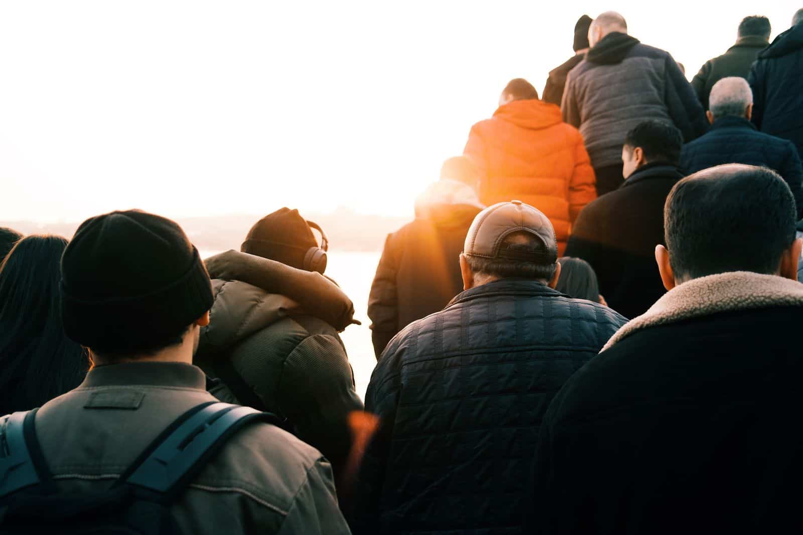 Group of people walking towards the sunrise wearing winter jackets, captured from behind. migration