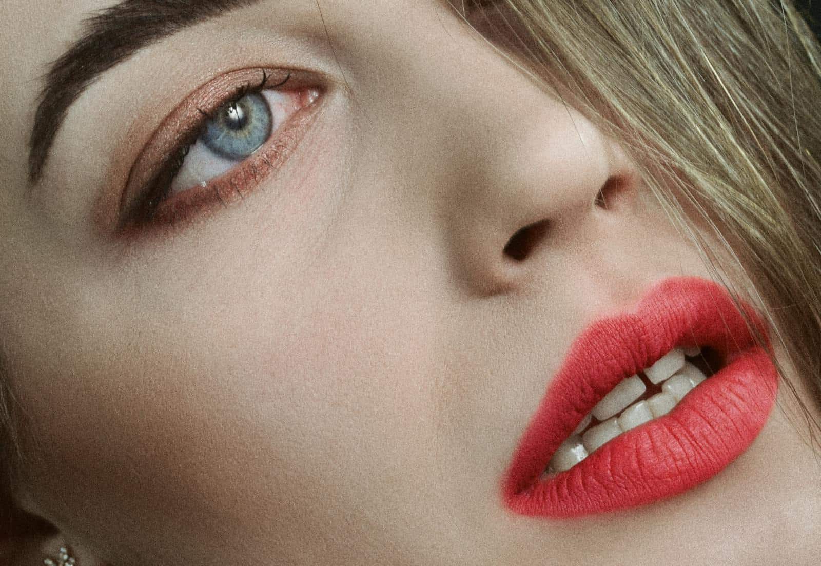 Intimate close-up shot showcasing vibrant red lipstick against fair skin with piercing blue eyes.