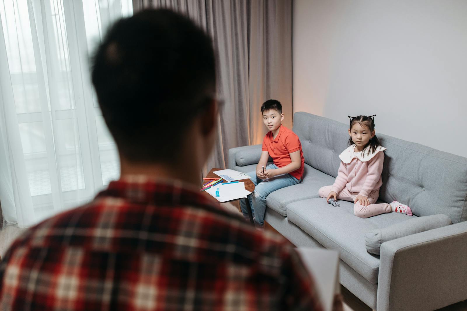 Kids sitting on couch with adult, engaging in educational activities in a cozy living room.