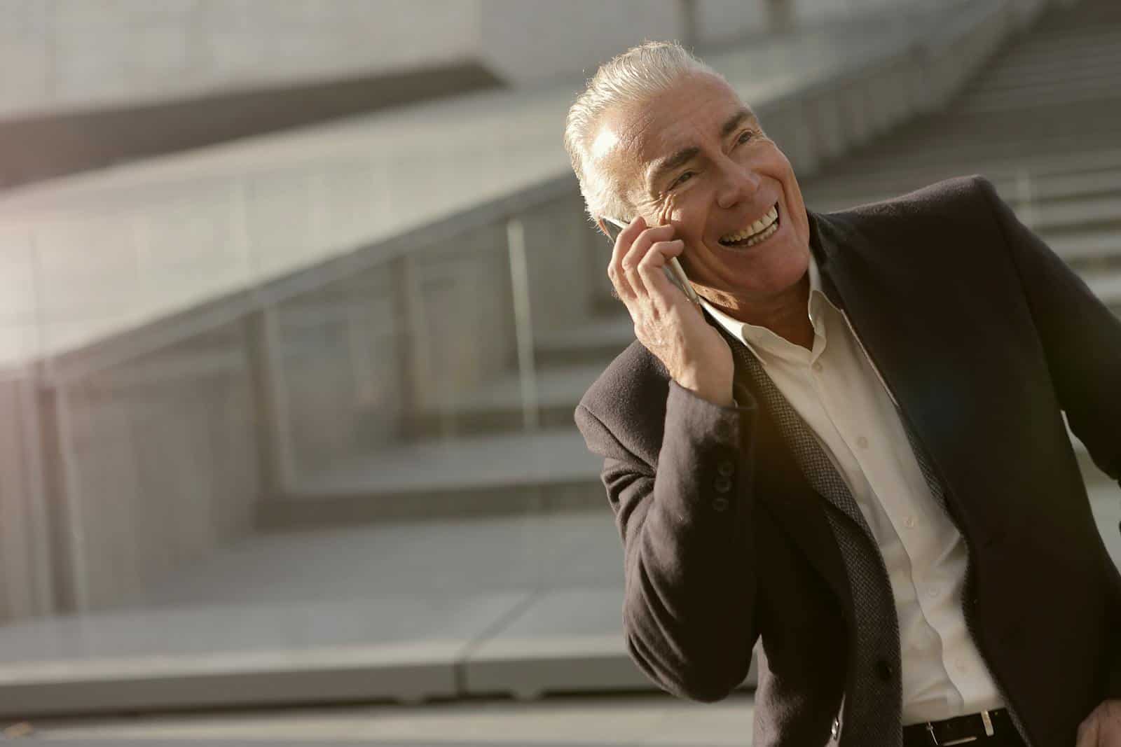 Senior businessman enjoying a mobile phone conversation outdoors with a smile.