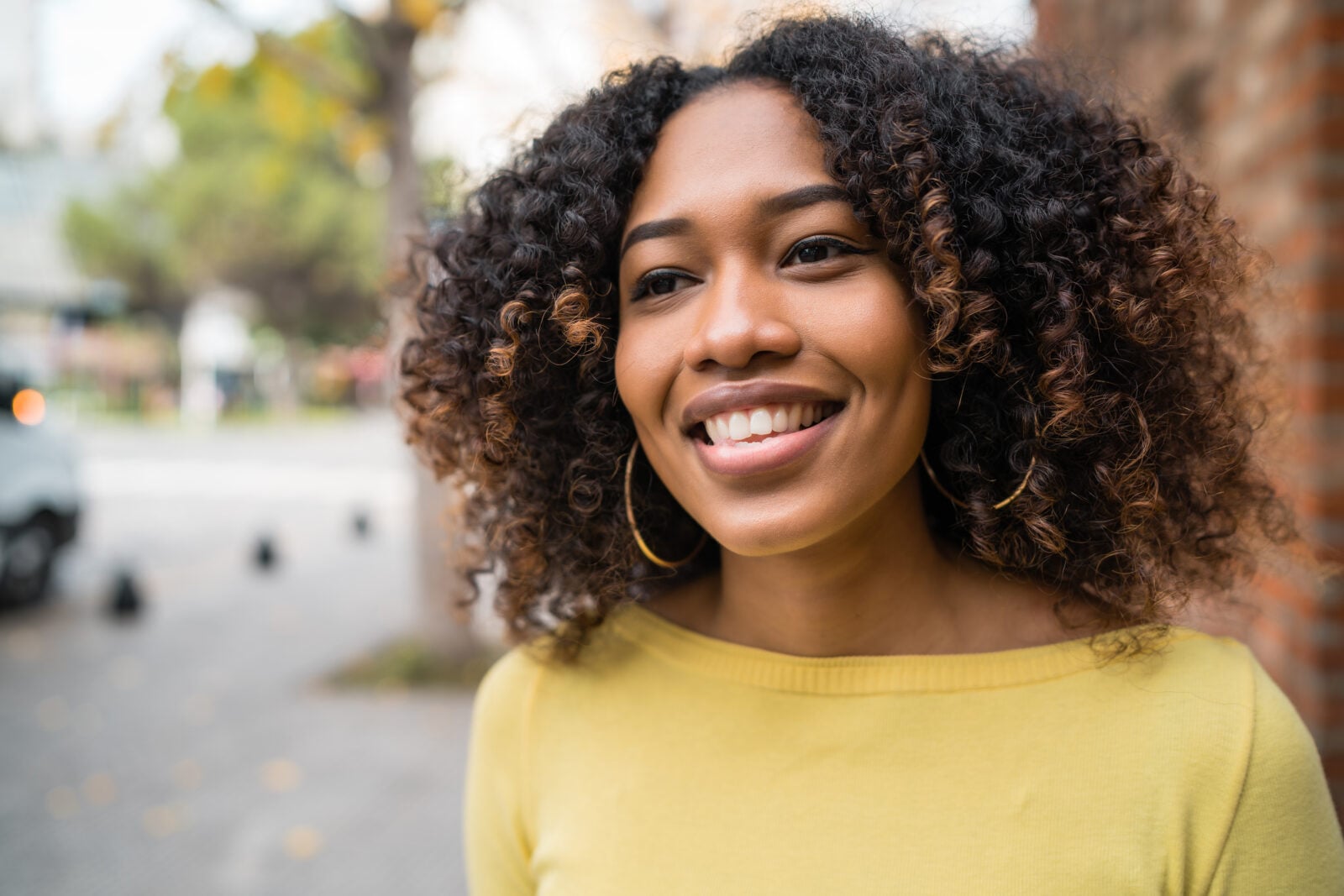 Portrait of beautiful young woman with curly hair standing outdoors in the street