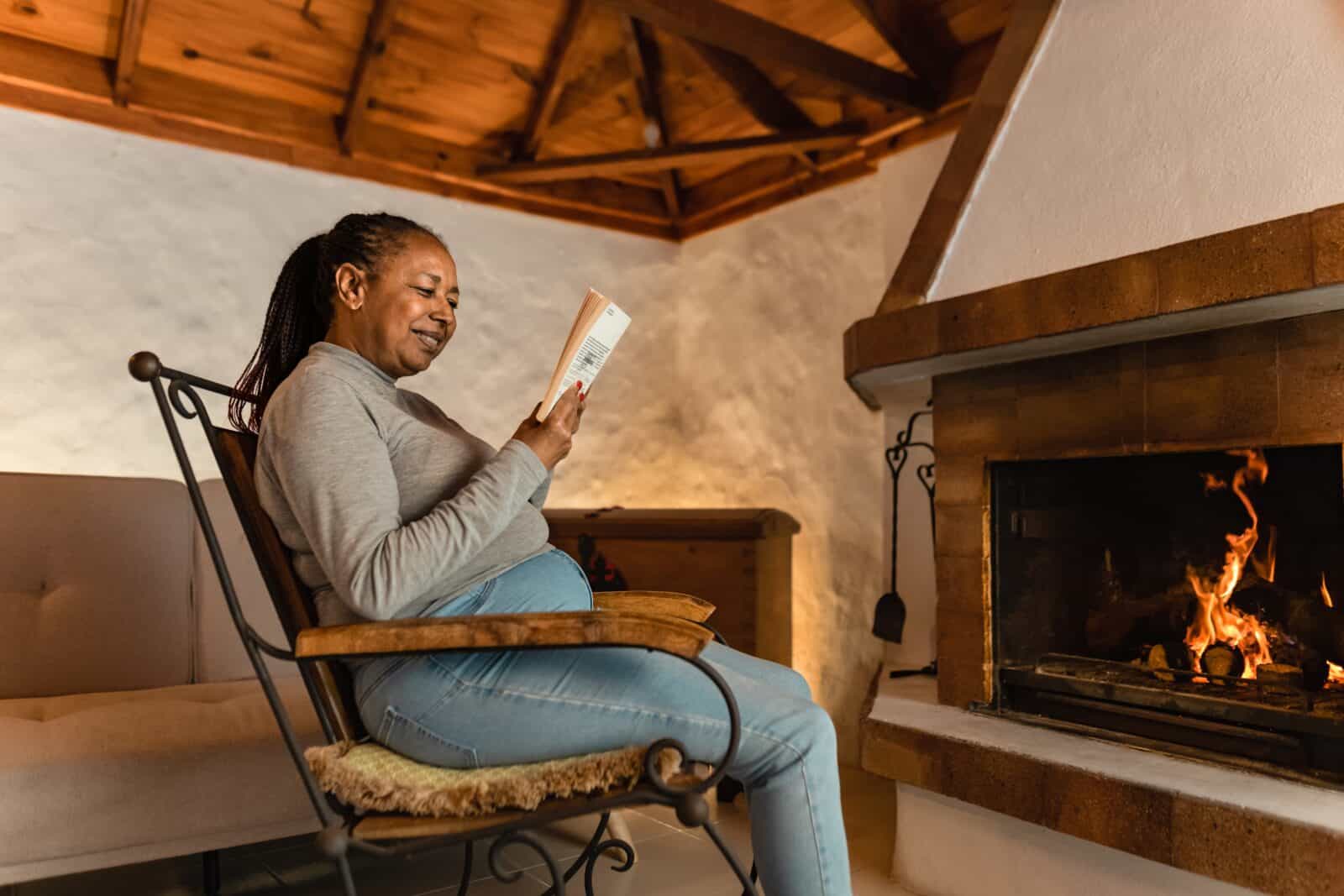 Senior woman reading while enjoying the fireplace
