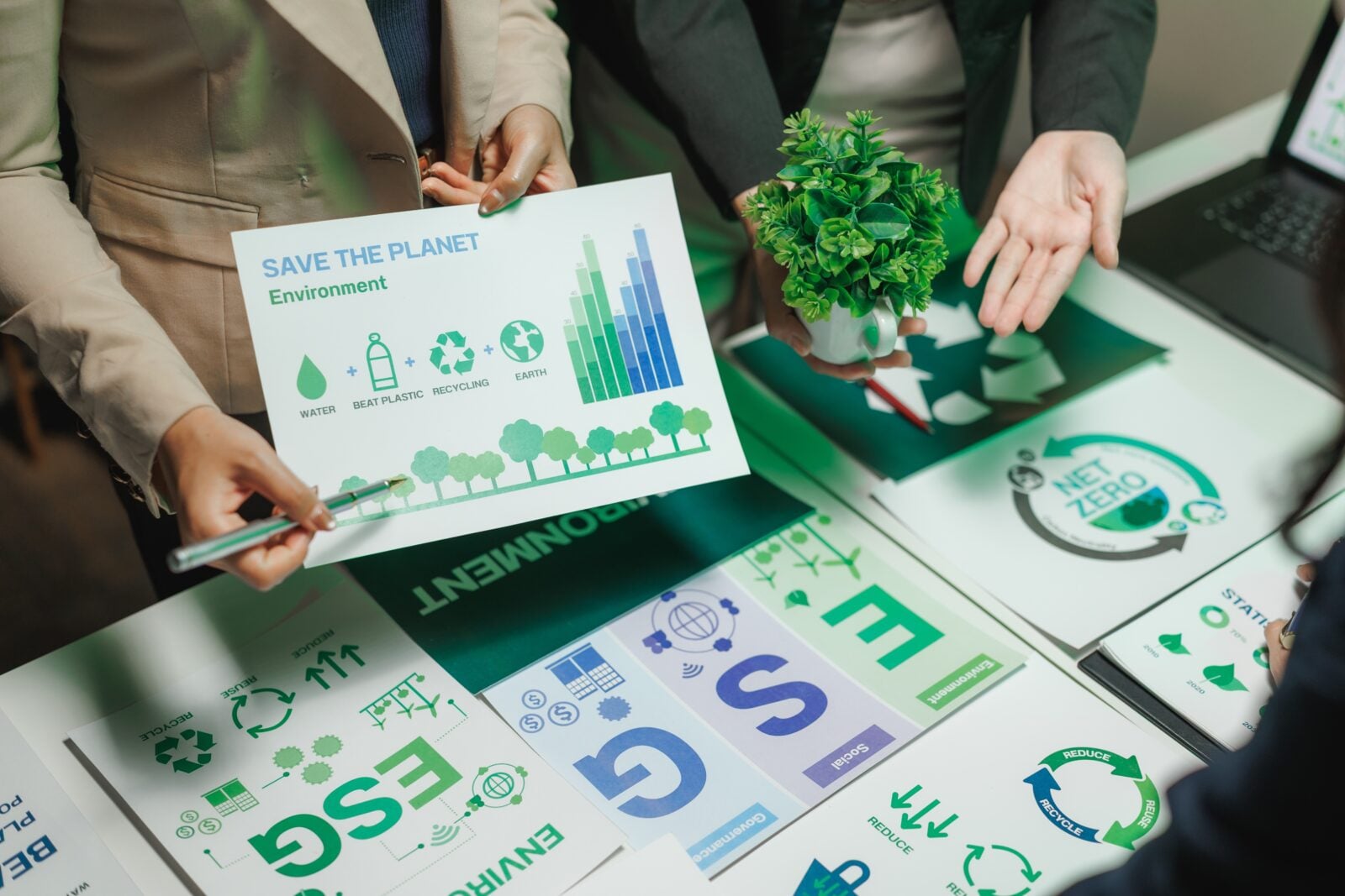 Business people collaborating and pointing at charts focused on environmental issues, recycling initiatives, and esg goals in a strategic meeting
