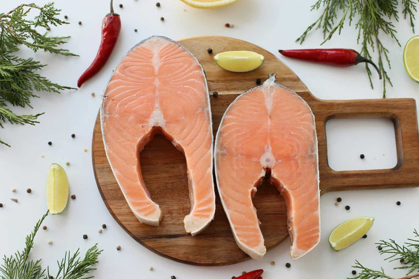 Top view of raw salmon steaks with lemon and herbs on a wooden board, ready for cooking.