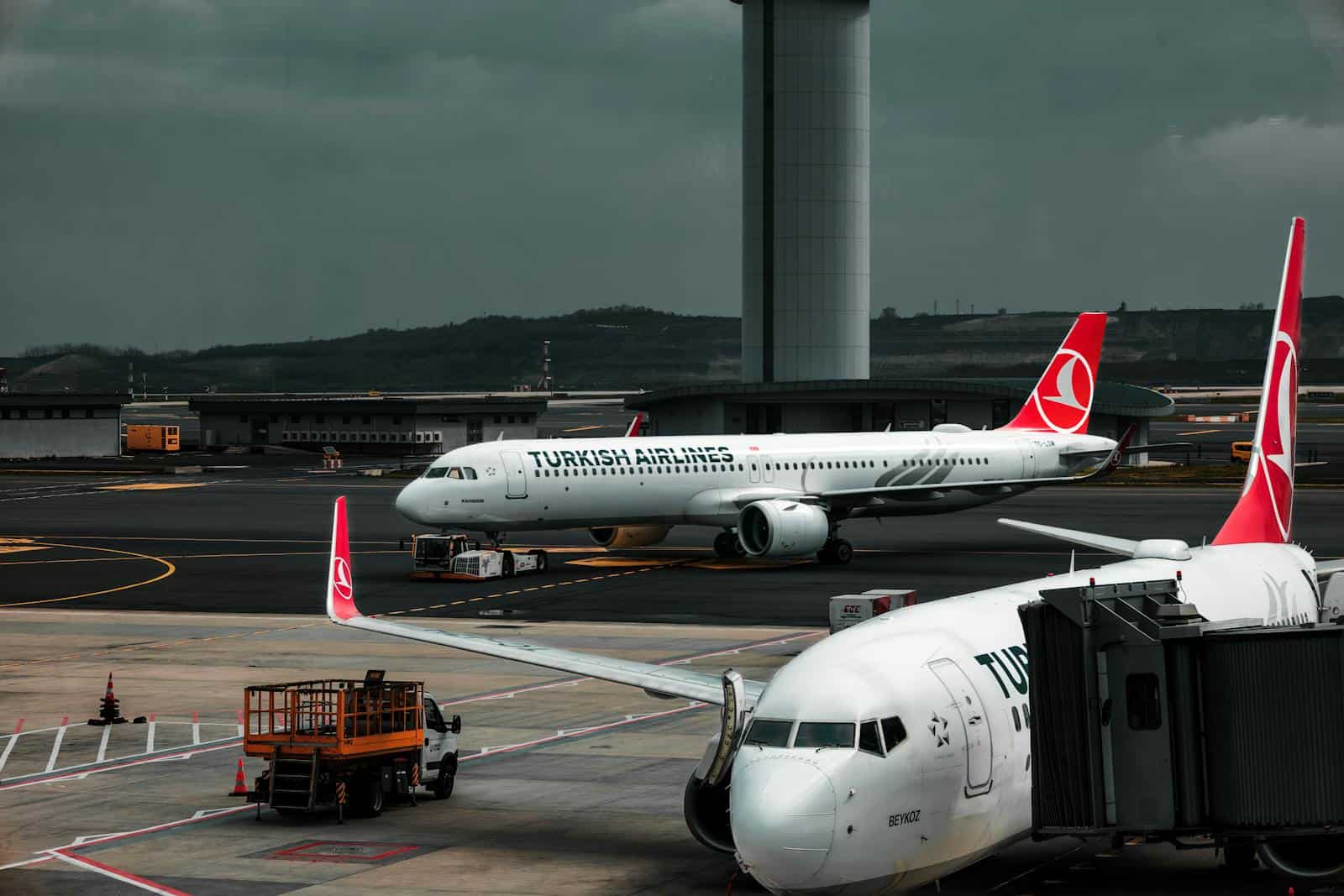 Turkish Airlines planes parked at an airport with a control tower in the background.