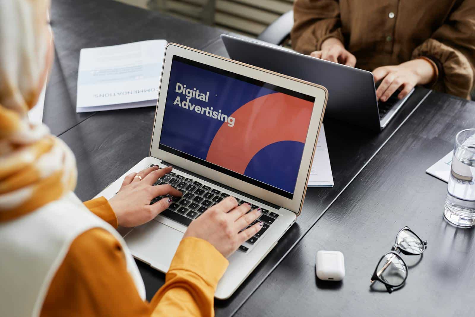 Two professionals work on laptops focusing on digital advertising in an office setting. Digital Marketing Manager