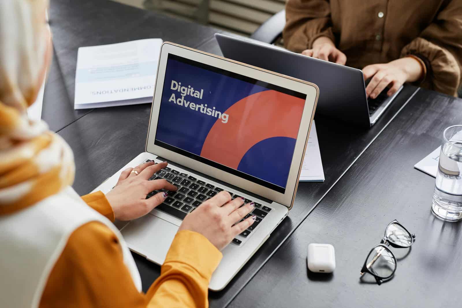 Two professionals work on laptops focusing on digital advertising in an office setting. Digital Marketing Manager