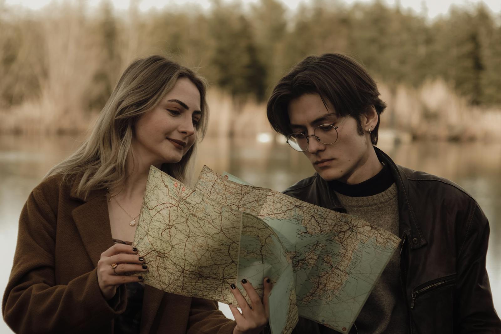 Young couple analyzing a map by a serene lake, planning their travel route in a tranquil nature setting.
