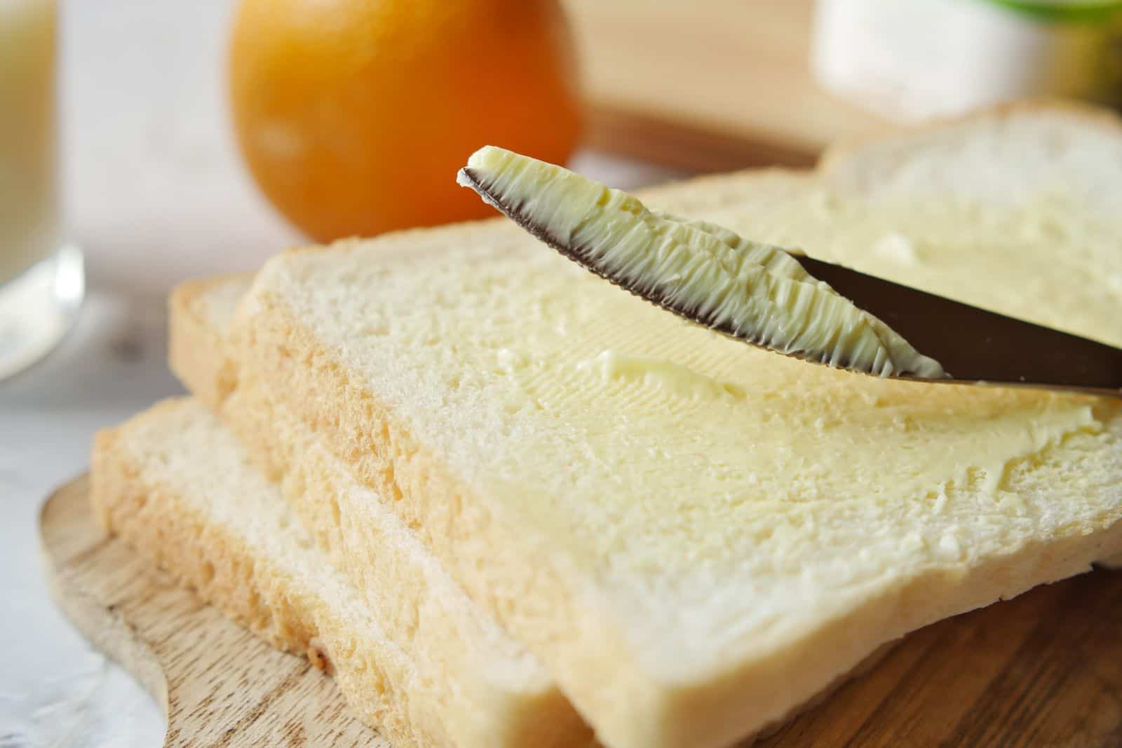A close-up view of butter being spread on a slice of bread, perfect for breakfast scenes. Margarine Vegetable Spreads