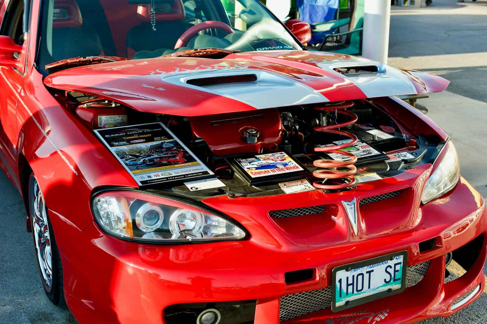A detailed look at a customized red Pontiac with an open hood showcasing its engine at a car event in Winnipeg.