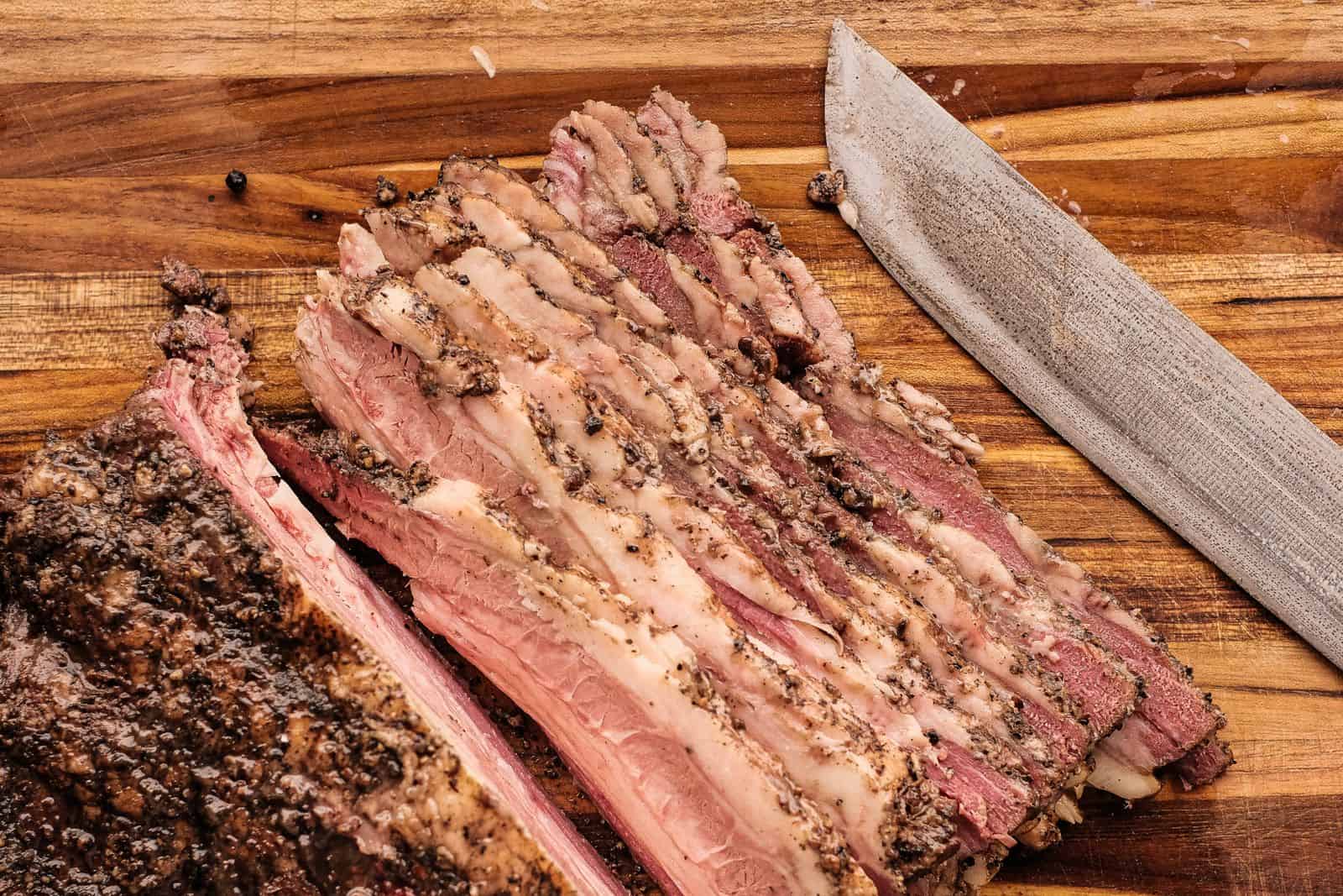 A detailed view of sliced brisket on a wooden cutting board with a knife. Beef Brisket