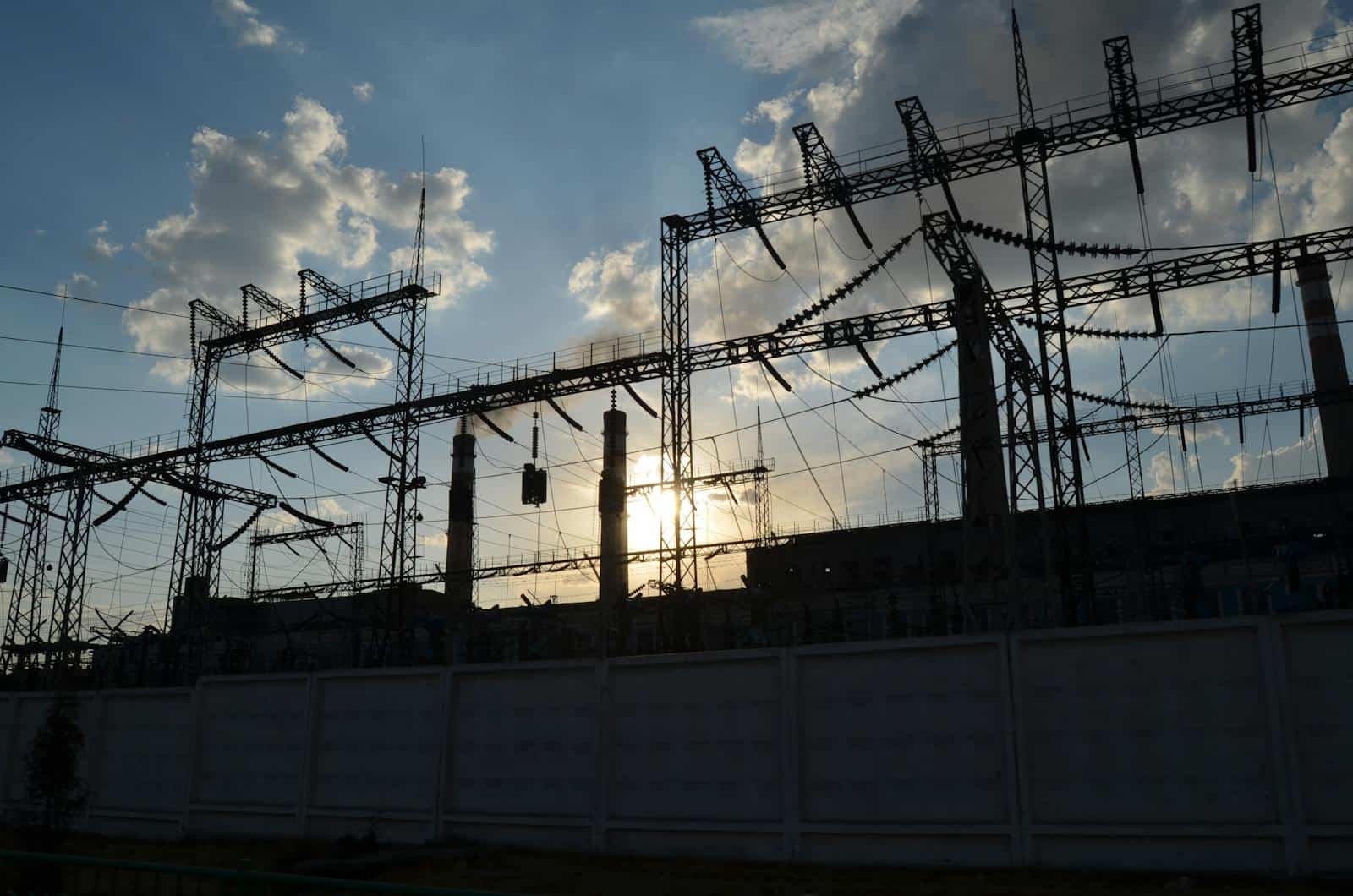 A striking silhouette of an electrical substation with the sun rising behind it, creating a dramatic sky. Electricity Grids