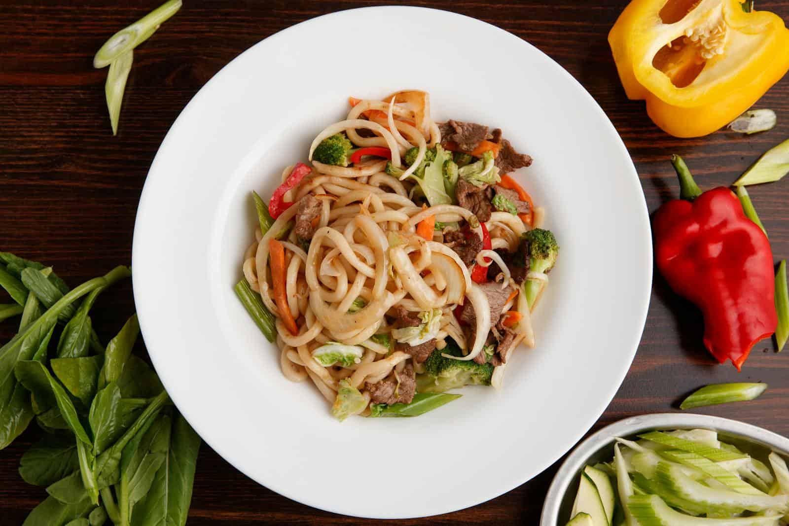 Appetizing stir-fried beef with noodles and fresh vegetables in a white plate.