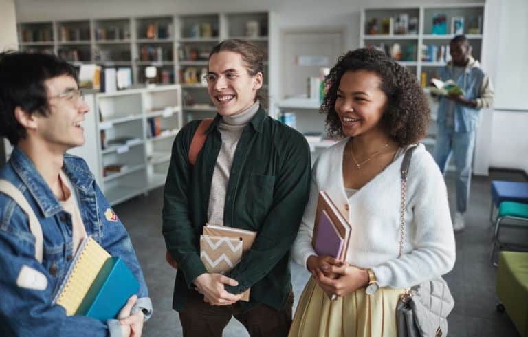 Group of diverse students laughing and holding books in a library environment.