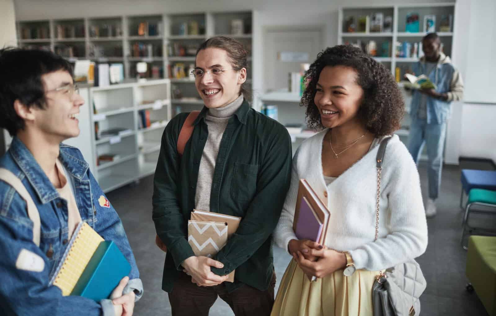 Group of diverse students laughing and holding books in a library environment.