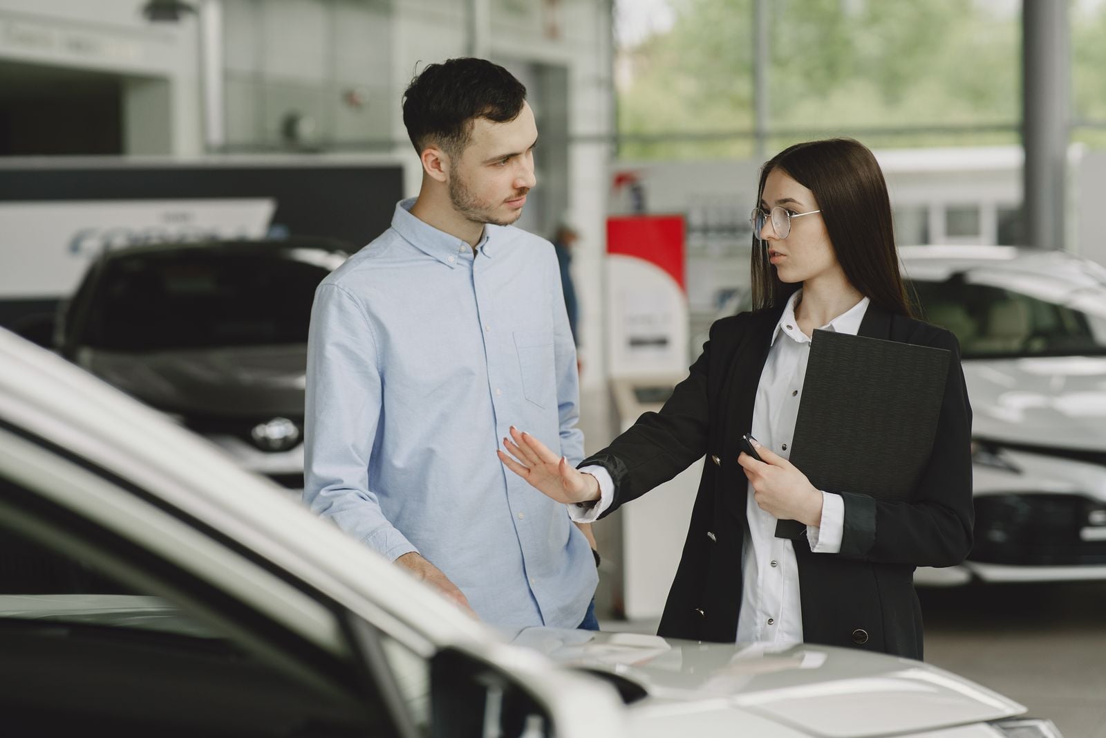 A salesperson and customer discussing car features in a dealership setting. buy car