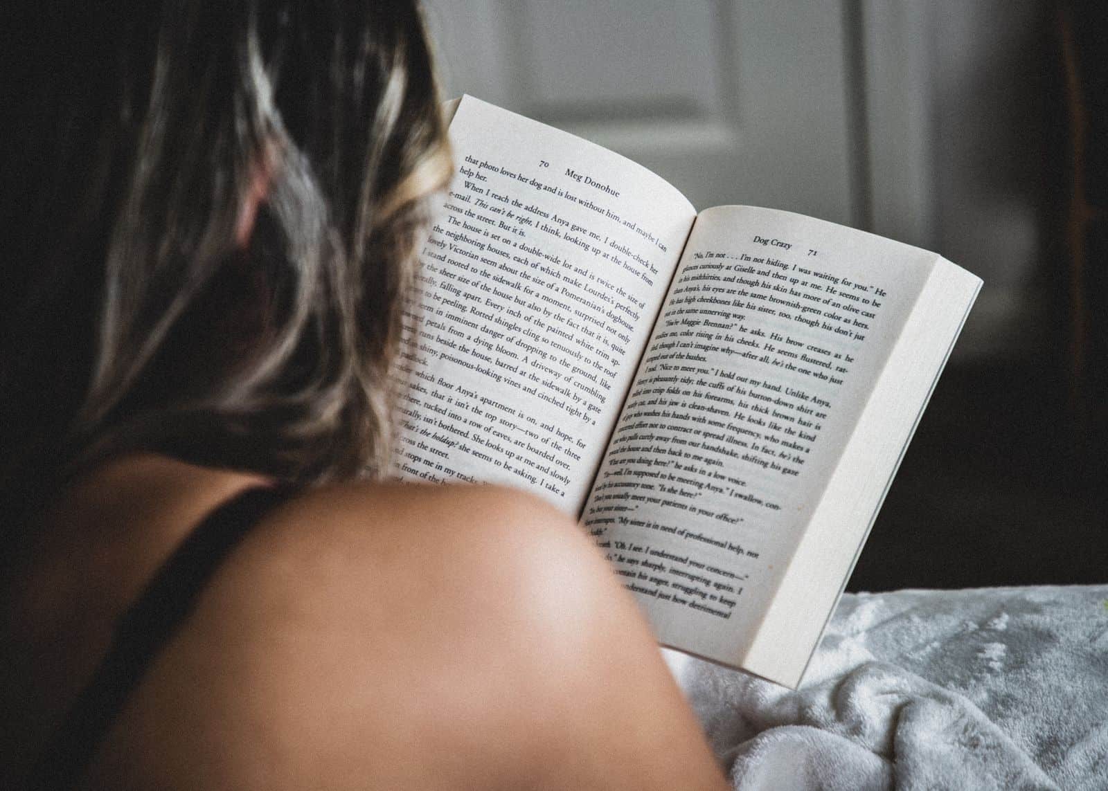 A woman reads a novel in bed, enjoying a quiet moment indoors, showcasing relaxation and literature.