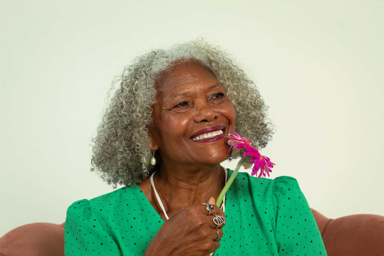 Portrait of a joyful elderly woman in green with a pink flower, exuding happiness.